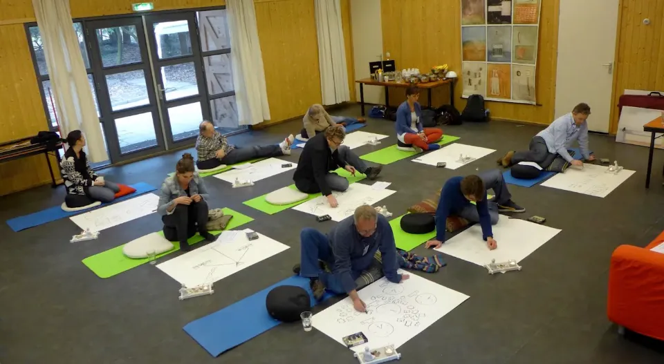 Participants working on drawings on mats on the floor of a meeting room