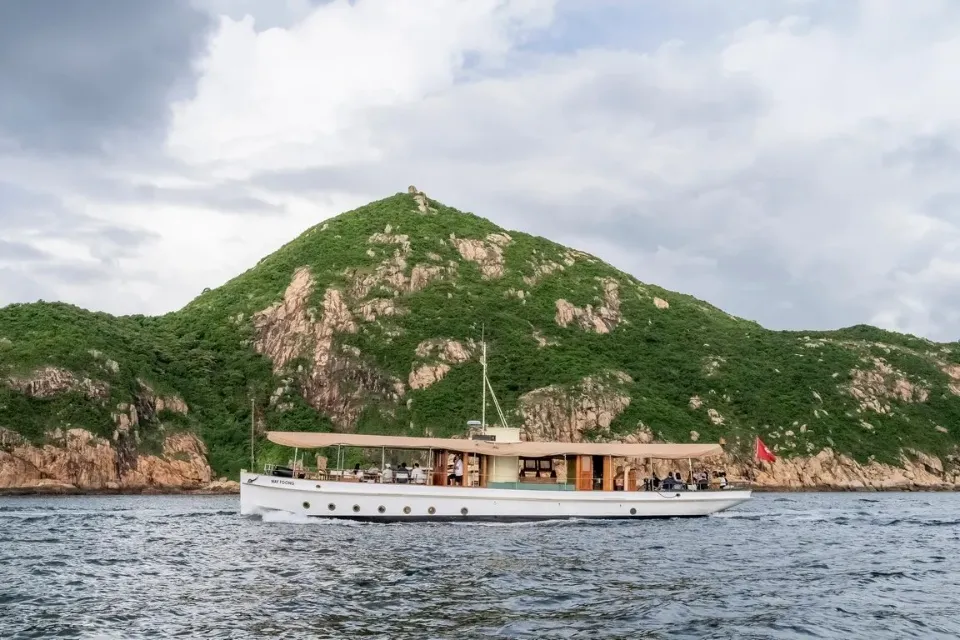Wayfoong on the water below a green hill