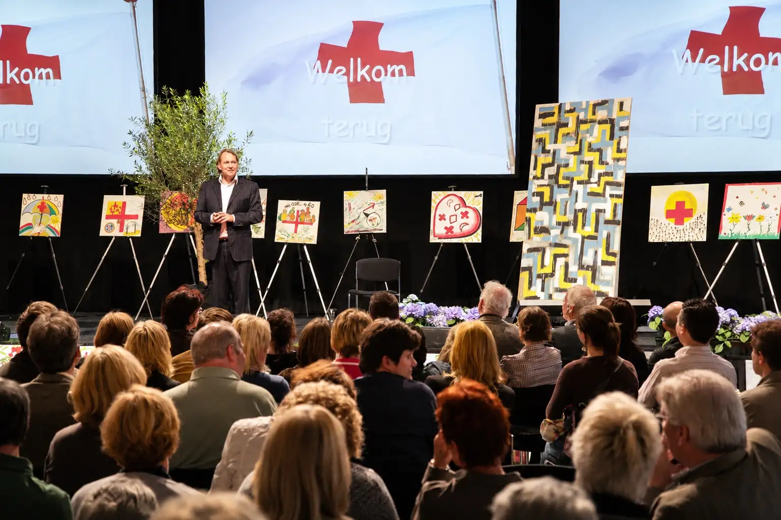 Speaker on a stage in front of an audience, with artworks on easels