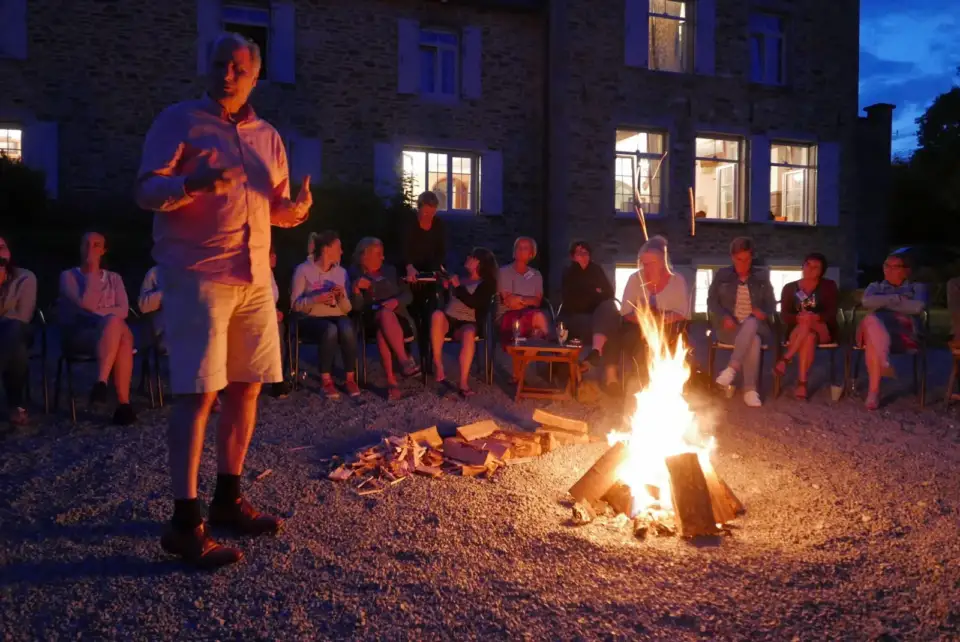Speaker beside a campfire in the evening, with an audience seated around it