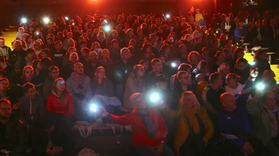 Audience in a dark hall holding up their phone lights