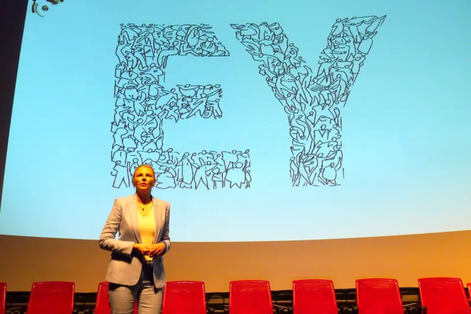 Speaker on stage in front of a large hand-drawn EY logo