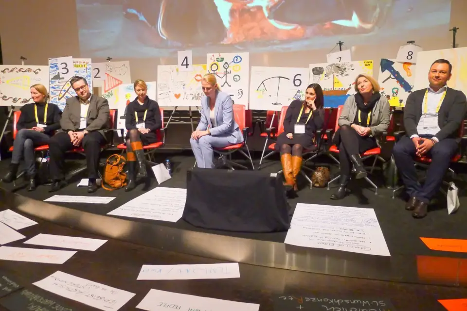Panellists seated on stage beside numbered cards