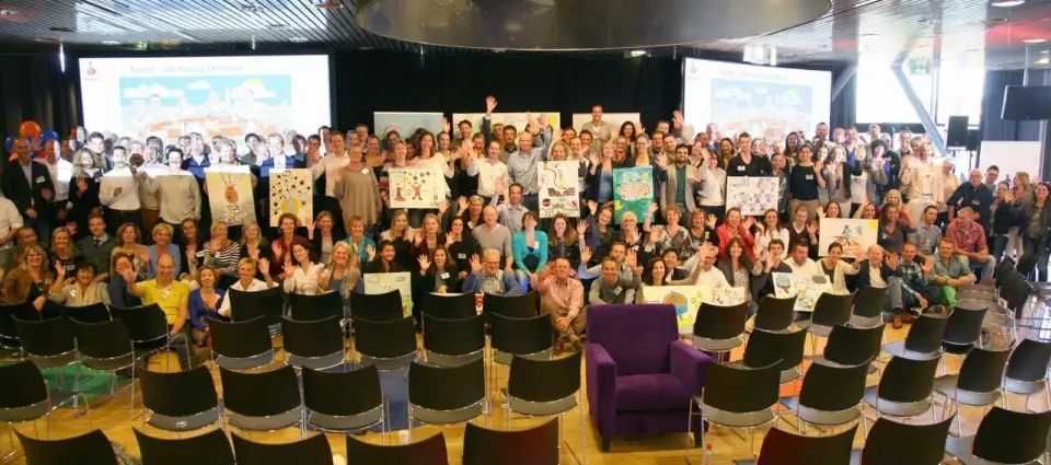 Large group of Rabobank employees holding up their drawings in a hall