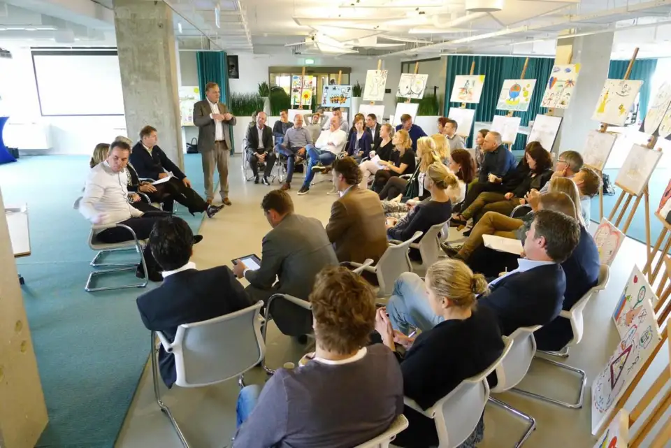 Participants seated in rows in an office space with artworks on easels