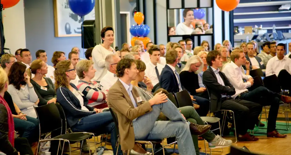 Audience listening in a hall decorated with orange and blue balloons