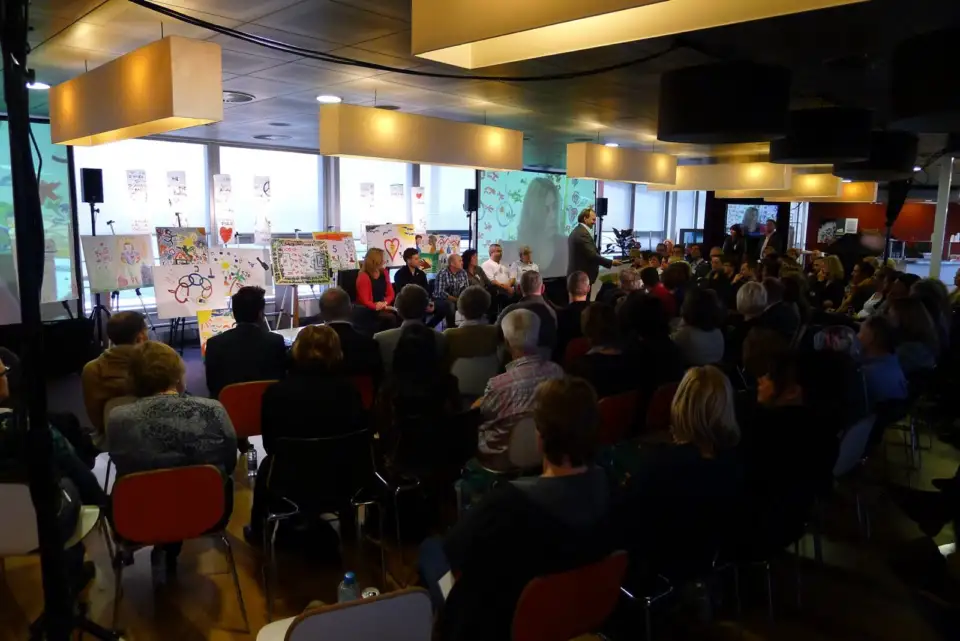 Packed hall of participants, with artworks on the walls
