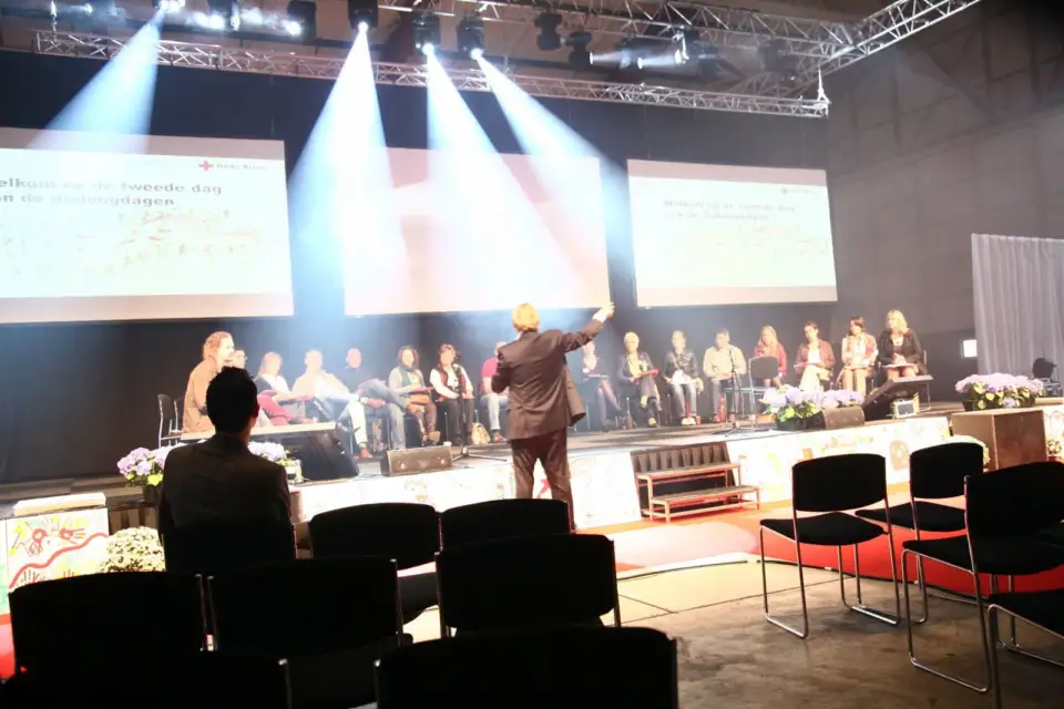 Speaker on stage pointing towards a seated panel