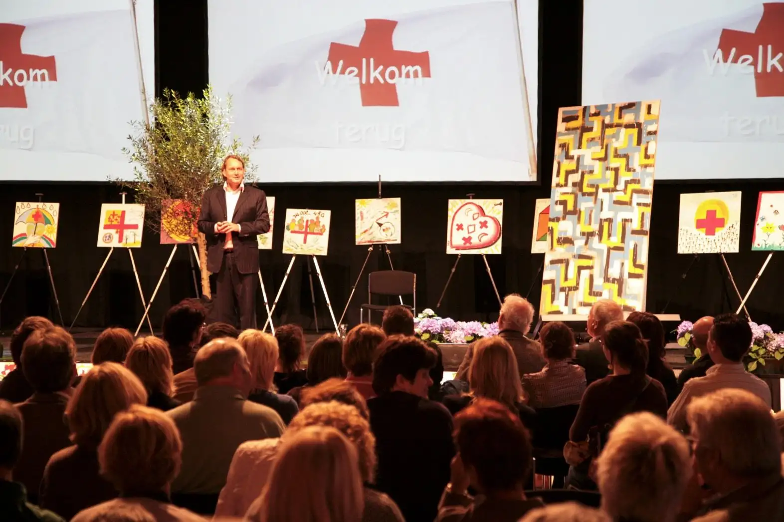 Speaker on a stage in front of an audience, with artworks on easels