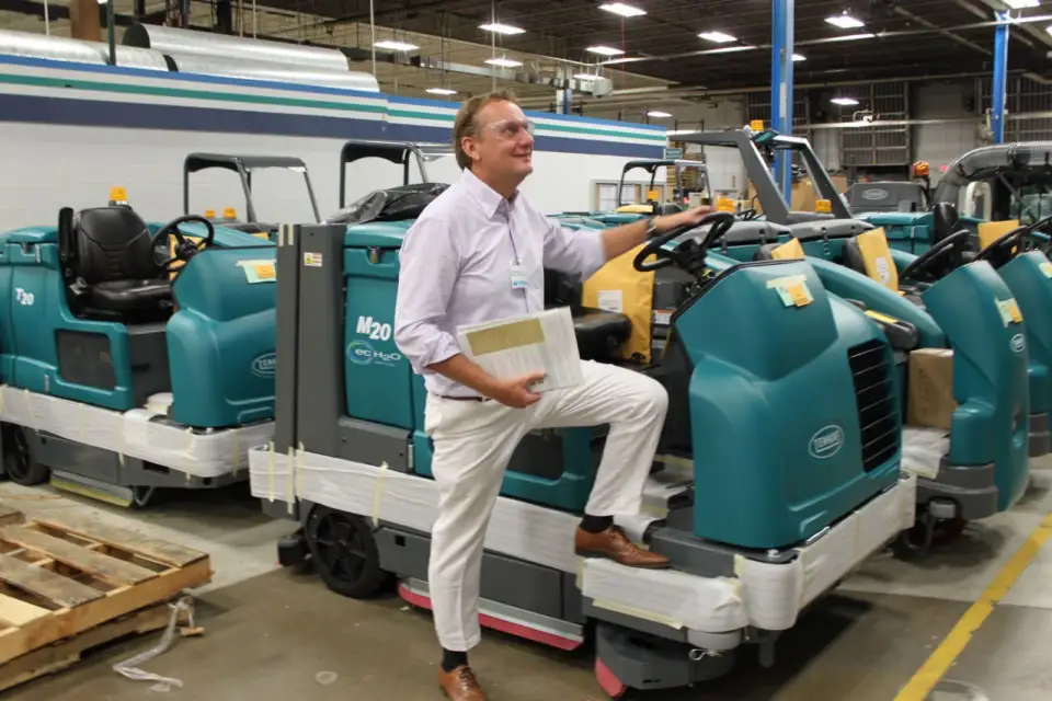 Man in a white suit holding a document beside Tennant floor-cleaning machines