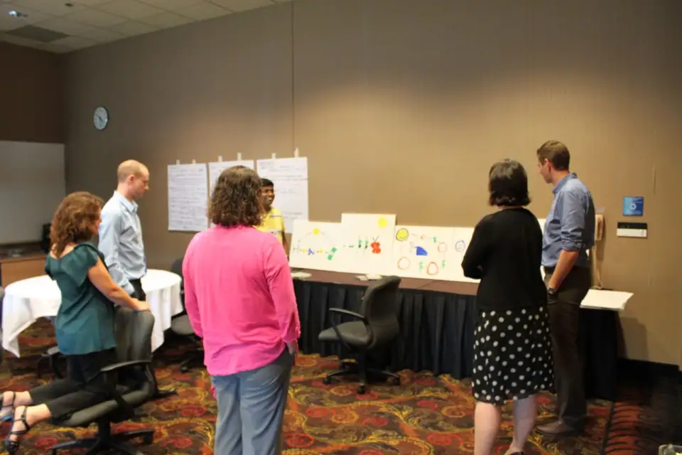 Participants standing at tables with drawings in a meeting room