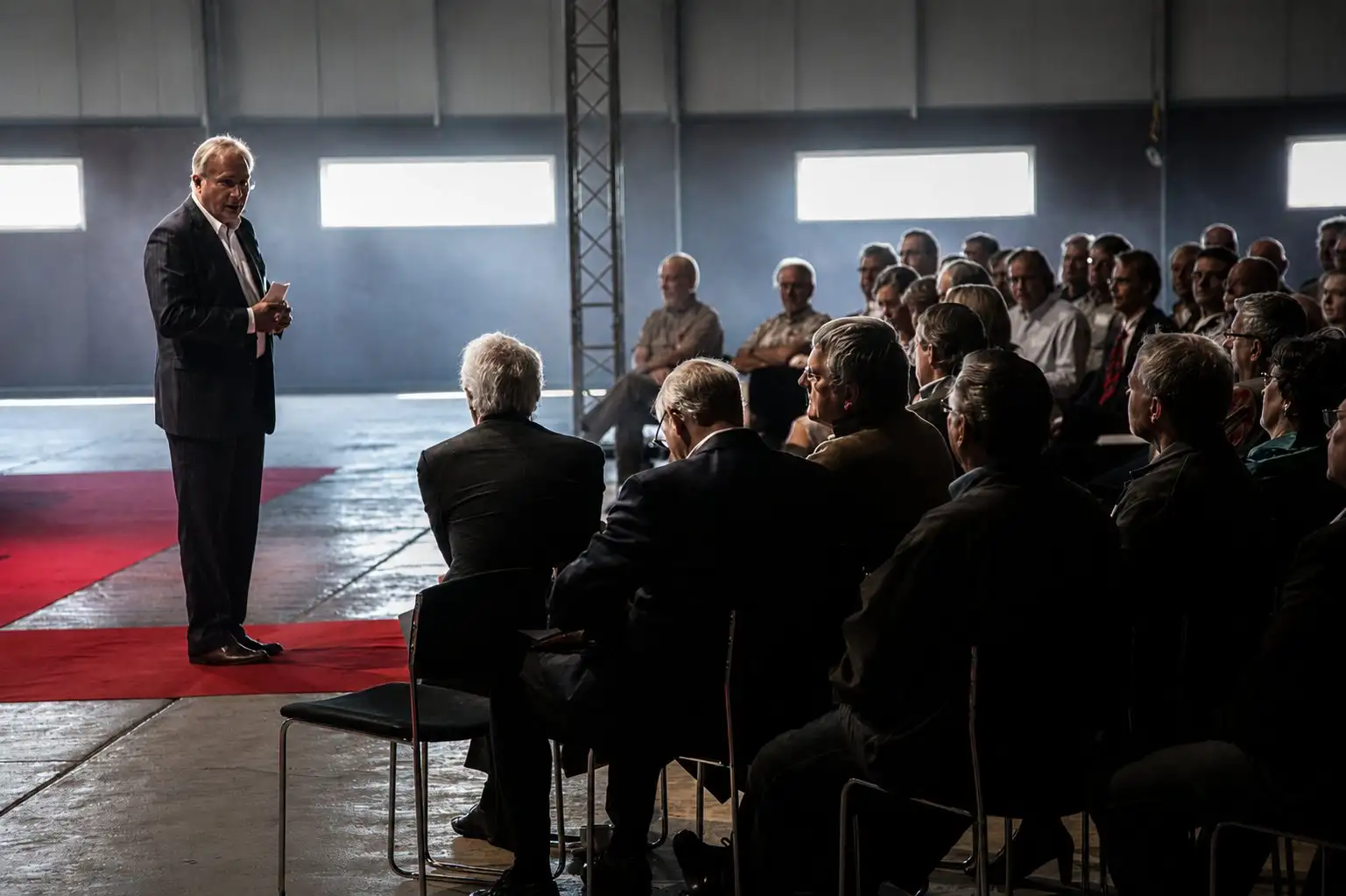 Speaker addressing a large audience in a darkened hall