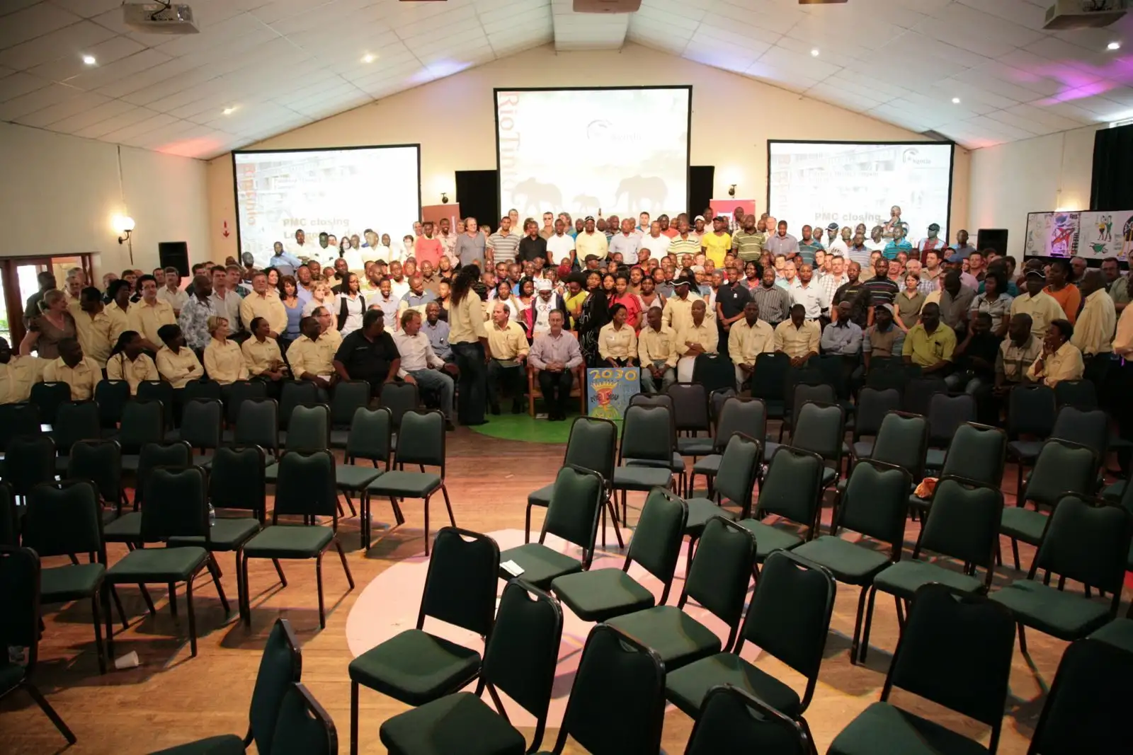Hall filled with participants in matching shirts, facing three screens