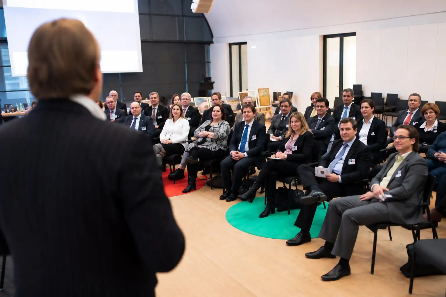 Speaker addresses executives seated in a circle around a green and red floor mat