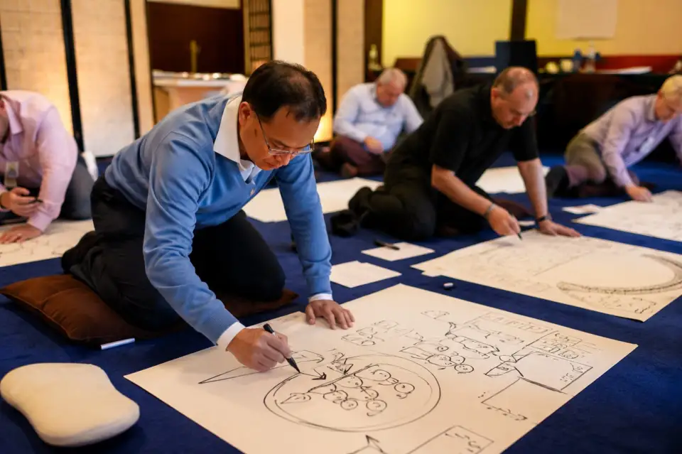 Participants kneeling on the floor, drawing on large sheets of paper during a dialogue session